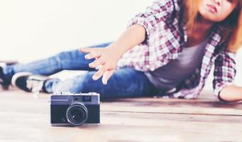 Young hipster photographer woman taking photo and look at camera sitting on wooden floor.