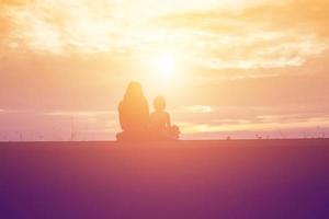 a silhouette of a happy young girl child the arms of his loving mother for a hug, in front of the sunset in the sky on a summer day. photo