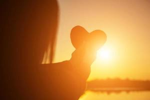 manos formando una forma de corazón con silueta de puesta de sol foto