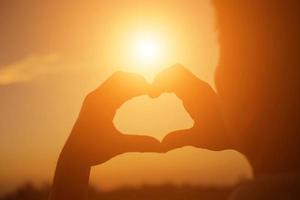 hands forming a heart shape with sunset silhouette photo