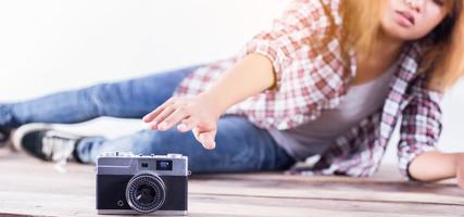 joven fotógrafa hipster tomando fotos y mirando la cámara sentada en el suelo de madera.