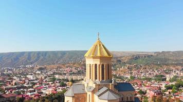 Panning aerial close up view exterior Tbilisi cathedral architecture with city panorama in sunny day. Aerial view of Holy Trinity Cathedral of Tbilisi Georgia sunset drone footage video