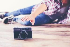 Young hipster photographer woman taking photo and look at camera sitting on wooden floor.