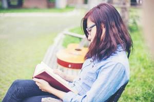 chica encantadora hipster relajándose en el parque mientras lee un libro, disfruta de la naturaleza. foto