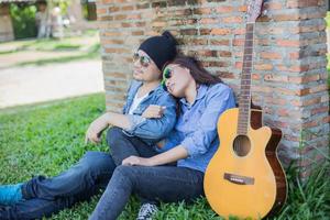 Hipster man playing guitar for his girlfriend outdoor against brick wall, enjoying together. photo