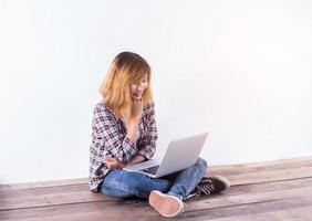 joven hipster sentada en el suelo de madera con las piernas cruzadas y usando una laptop con fondo blanco foto