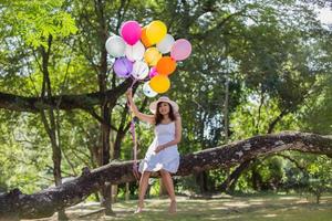 Young teen girl sitting on tree and holding balloons in hand photo