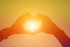 hands forming a heart shape with sunset silhouette photo