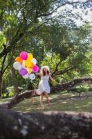 Young teen girl sitting on tree and holding balloons in hand photo