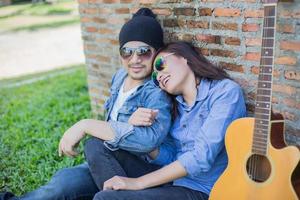 Hipster man playing guitar for his girlfriend outdoor against brick wall, enjoying together. photo