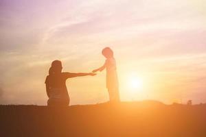 Mother encouraged her son outdoors at sunset, silhouette concept photo