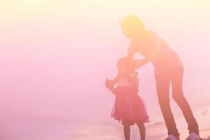 a silhouette of a happy young girl child the arms of his loving mother for a hug, in front of the sunset in the sky on a summer day. photo