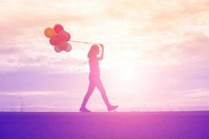 silhouette of young woman holding colorful of balloons with sunset photo