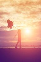 silhouette of young woman holding colorful of balloons with sunset photo