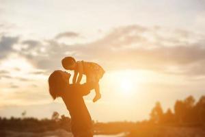 una silueta de una niña feliz los brazos de su madre amorosa para un abrazo, frente a la puesta de sol en el cielo en un día de verano. foto