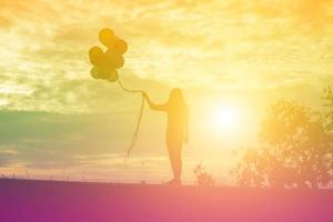 silueta de mujer joven sosteniendo coloridos globos con puesta de sol foto