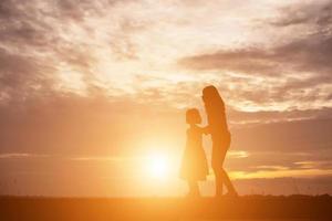 a silhouette of a happy young girl child the arms of his loving mother for a hug, in front of the sunset in the sky on a summer day. photo