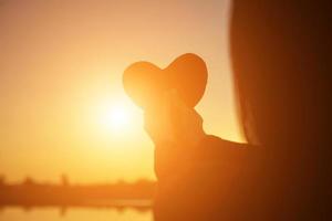 manos formando una forma de corazón con silueta de puesta de sol foto