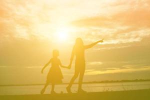 a silhouette of a happy young girl child the arms of his loving mother for a hug, in front of the sunset in the sky on a summer day. photo