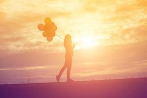 silueta de mujer joven sosteniendo coloridos globos con puesta de sol foto