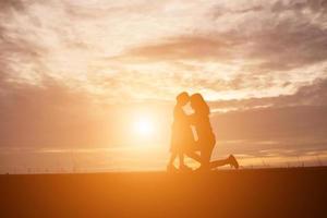 a silhouette of a happy young girl child the arms of his loving mother for a hug, in front of the sunset in the sky on a summer day. photo