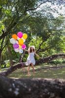 joven adolescente sentada en un árbol y sosteniendo globos en la mano foto