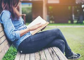 Hipster charming girl relaxing in the park while read book, Enjoy nature around. photo