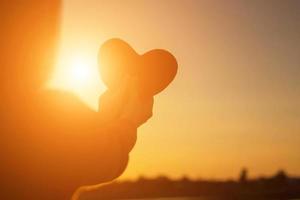 hands forming a heart shape with sunset silhouette photo