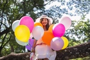 Young teen girl sitting on tree and holding balloons in hand photo