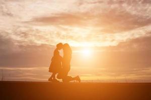 a silhouette of a happy young girl child the arms of his loving mother for a hug, in front of the sunset in the sky on a summer day. photo