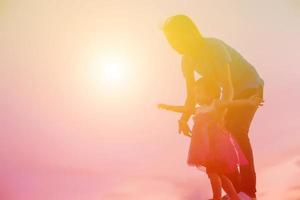 a silhouette of a happy young girl child the arms of his loving mother for a hug, in front of the sunset in the sky on a summer day. photo