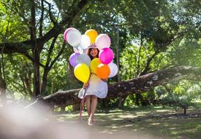 Young teen girl sitting on tree and holding balloons in hand photo