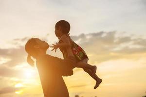a silhouette of a happy young girl child the arms of his loving mother for a hug, in front of the sunset in the sky on a summer day. photo