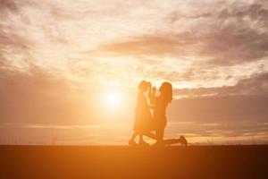 a silhouette of a happy young girl child the arms of his loving mother for a hug, in front of the sunset in the sky on a summer day. photo