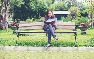 Hipster charming girl relaxing in the park while read book, Enjoy nature around. photo