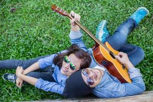 hombre hipster tocando la guitarra para su novia al aire libre contra la pared de ladrillo, disfrutando juntos. foto