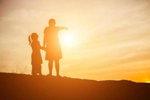 Mother encouraged her son outdoors at sunset, silhouette concept photo