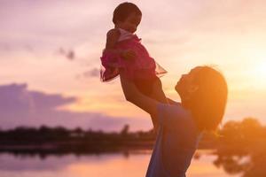 a silhouette of a happy young girl child the arms of his loving mother for a hug, in front of the sunset in the sky on a summer day. photo