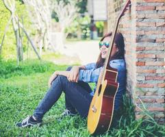 hombre hipster tocando la guitarra para su novia al aire libre contra la pared de ladrillo, disfrutando juntos. foto