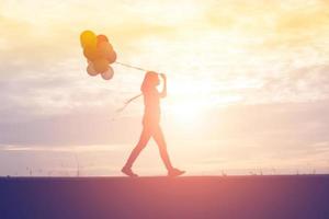 silueta de mujer joven sosteniendo coloridos globos con puesta de sol foto