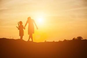 Mother encouraged her daughter out of the shadows at sunset. photo