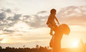 a silhouette of a happy young girl child the arms of his loving mother for a hug, in front of the sunset in the sky on a summer day. photo