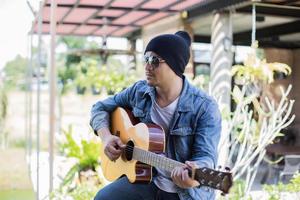 joven hipster tocando guitarra para relajarse en sus vacaciones, disfrutar con aire fresco y natural. foto