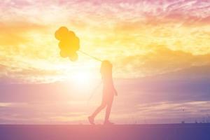 silueta de mujer joven sosteniendo coloridos globos con puesta de sol foto