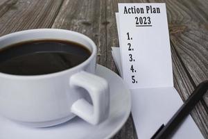 Note book with action plan 2023 text and coffee on wooden desk. photo