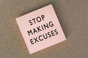 Stop making excuses text on sticky note against brown paper background. photo