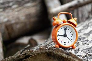 despertador naranja aislado en el tronco del árbol. el reloj puesto a las 9 en punto. foto
