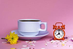 taza de café blanca con reloj despertador a las 8 en punto sobre fondo rosa. foto