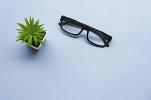Office desk with potted plant and glasses on blue background. Flat lay. photo