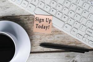Note with Sign Up Today stick on white keyboard on wooden desk with coffee. photo